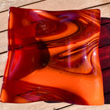 Large square glass bowl with wavy edges and a square center foot, viewed from above sitting on a slatted wood table, outside in sun light.