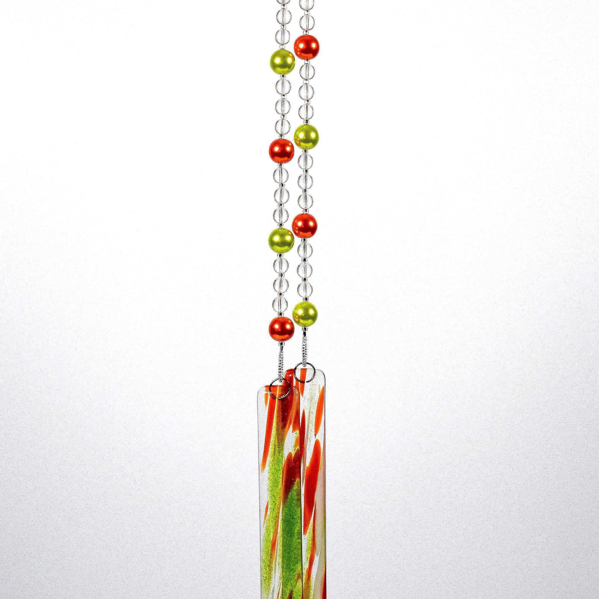 Two strings of glass beads hanging against white background, anchored by two pieces of green and orange fused glass.