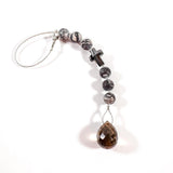 Small sun catcher hanging vertically against white background. Silver-gray crystal cross is flanked by six jasper stone beads in a marbled gray, anchored by large smoky quartz pendant.