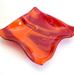 Large square glass bowl with wavy edges and a square center foot, viewed at an angle sitting on a white surface.