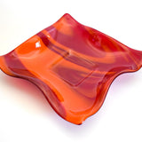 Large square glass bowl with wavy edges and a square center foot, viewed at an angle sitting on a white surface.