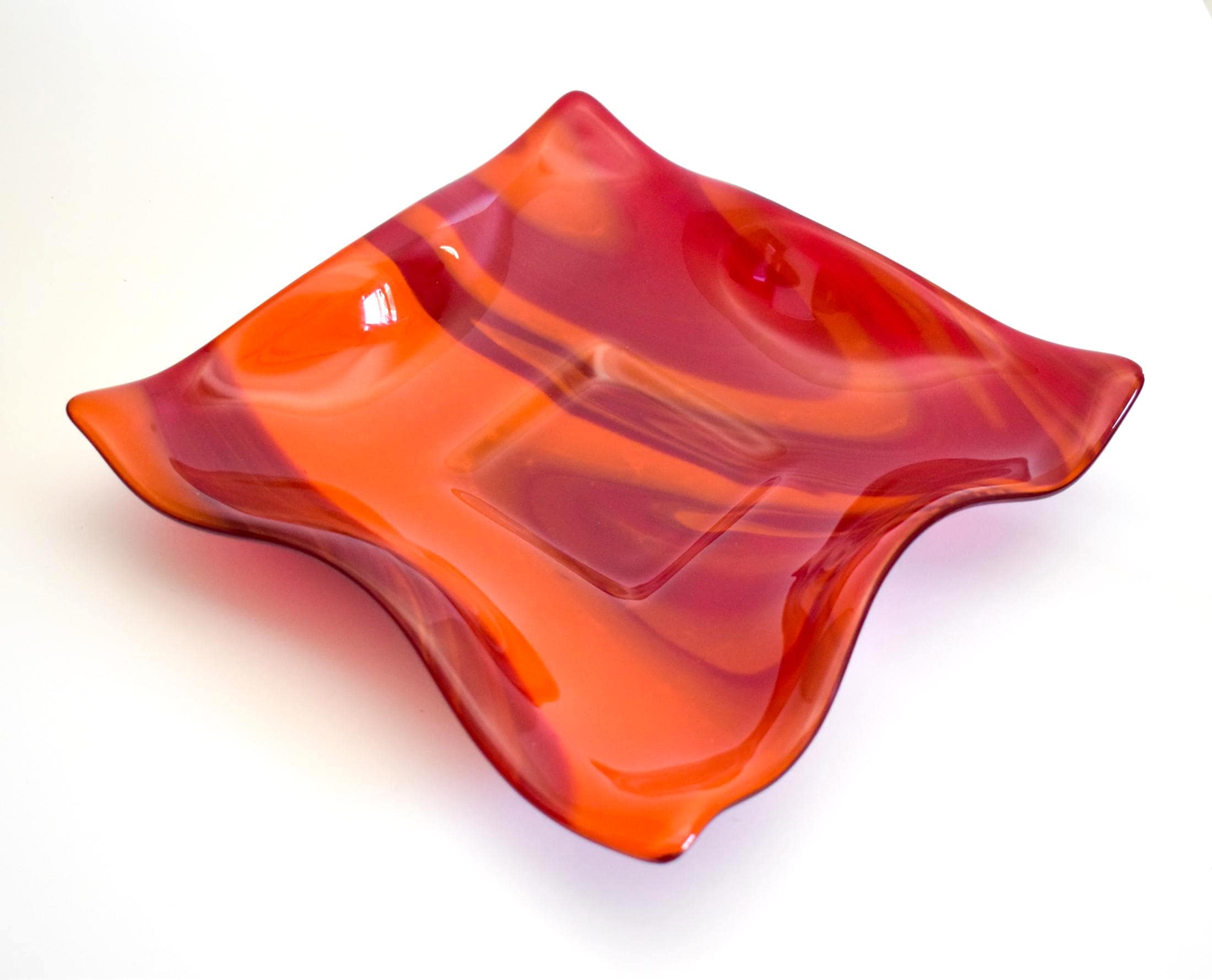 Large square glass bowl with wavy edges and a square center foot, viewed at an angle sitting on a white surface.