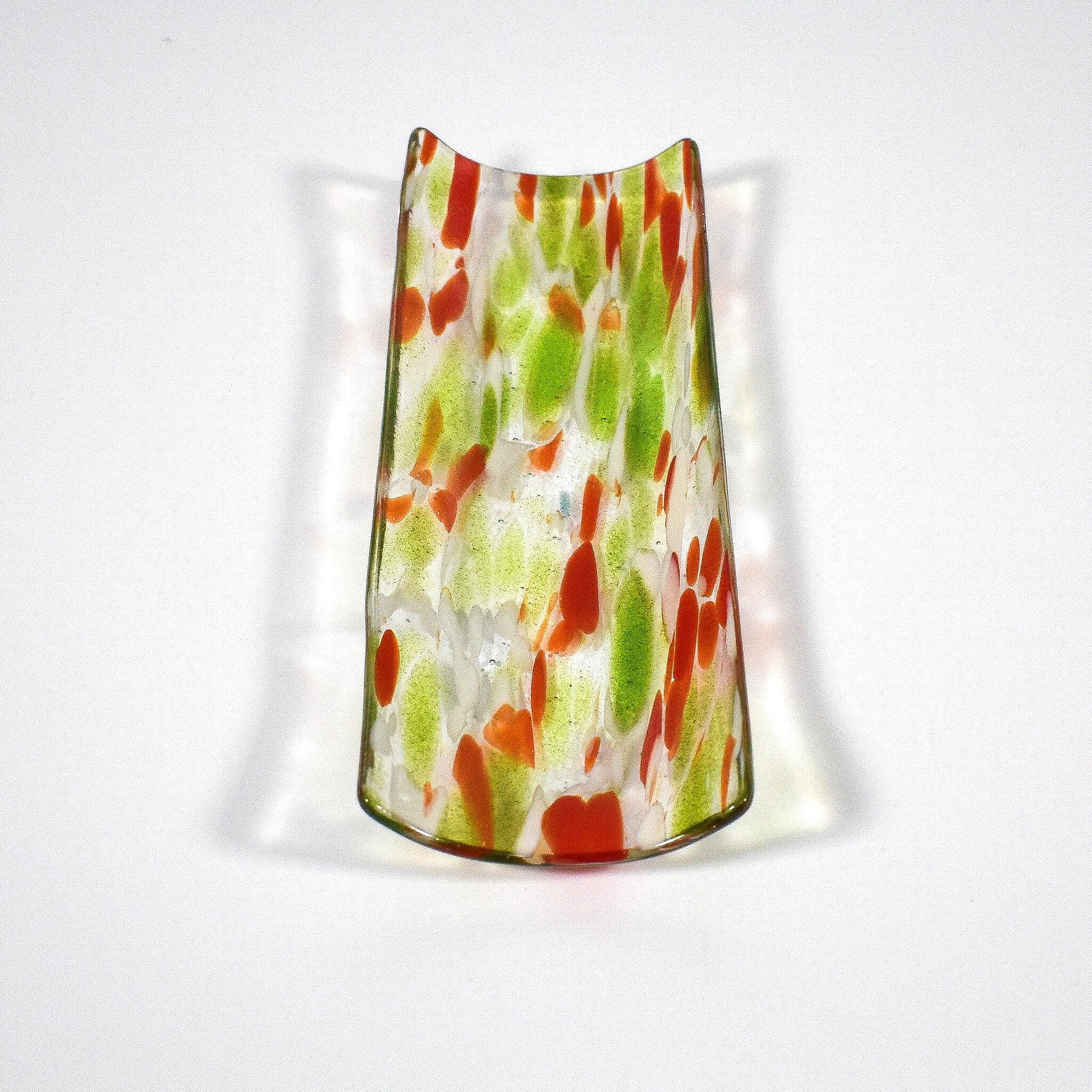 A decorative glass vase with a unique shape. The vase is clear with a pattern of red and green spots. The vase has a curved top and a wider base, creating a visually interesting design. The glass has a glossy finish.