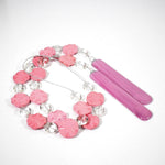 Pink magnesite stone wind chime made by Cinjo Handmade coiled on a white surface with 14 flat, wavy, round magnesite beads strung with oval glass crystal beads, strung on a single stainless steel wire with a piece of pink fused glass at each end.