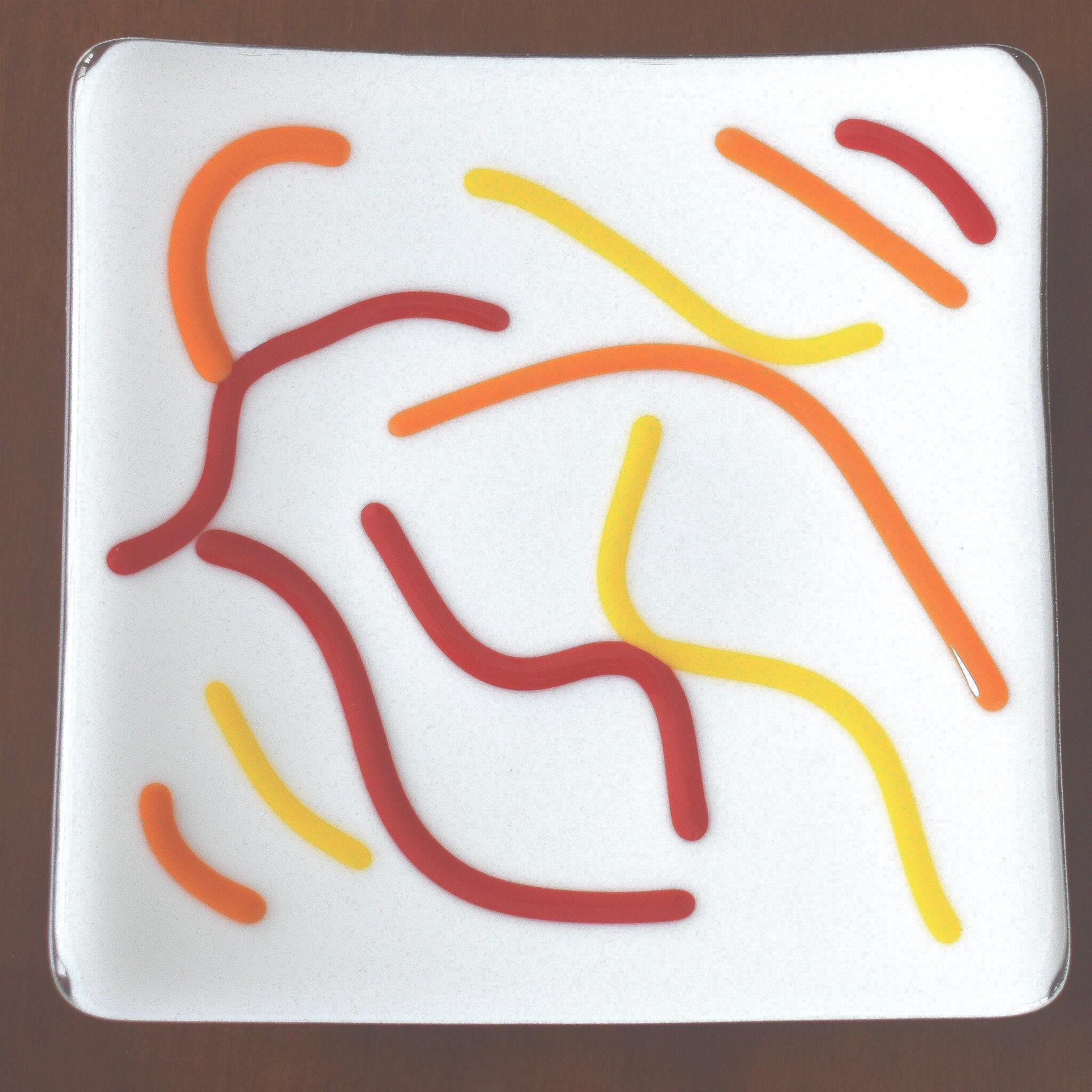 Close up view of orange, red and yellow abstract design on vanilla cream fused glass tray.