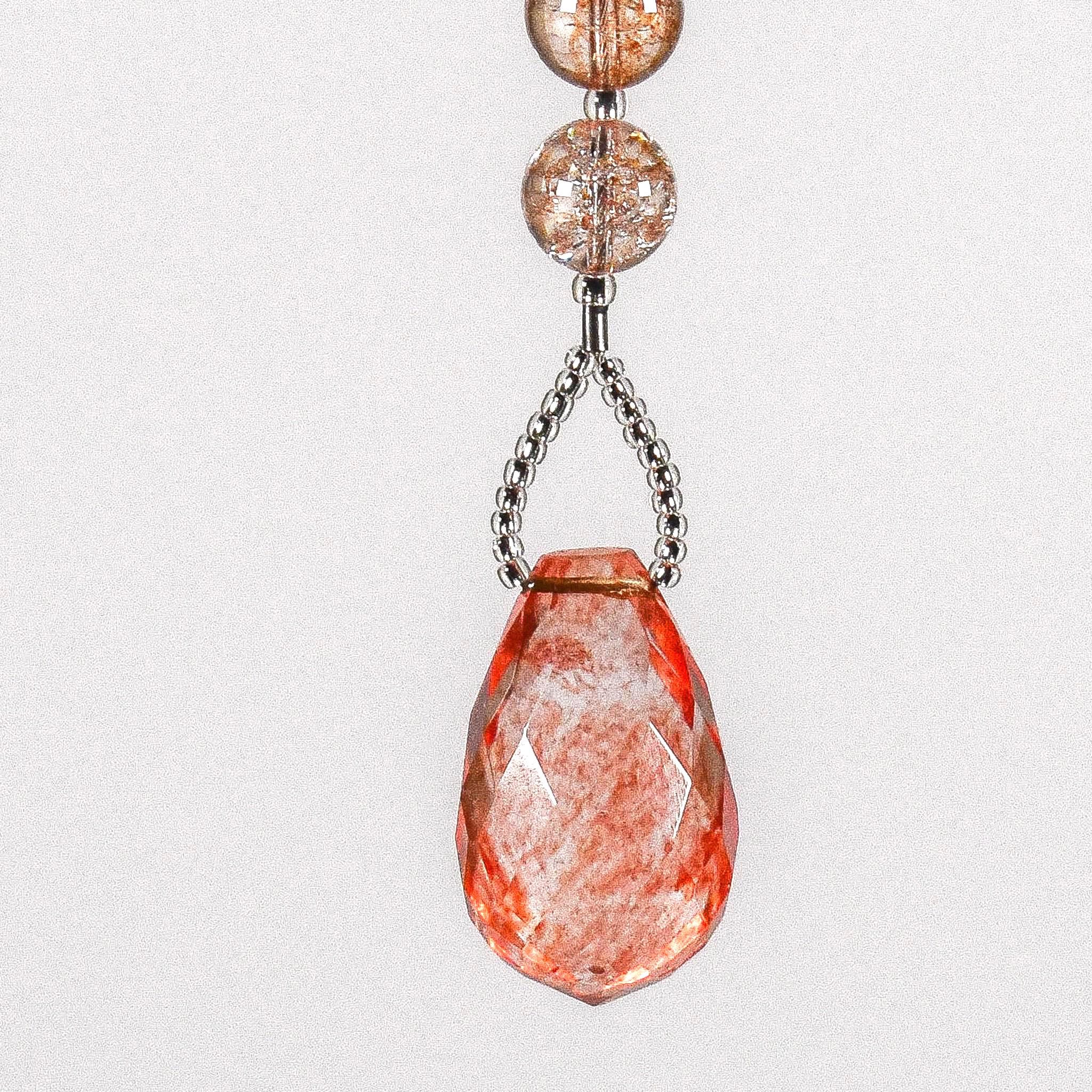 A teardrop-shaped pink and white crystal bead hanging from a wire chain that is covered with seed beads. The bead is faceted and has a translucent appearance.