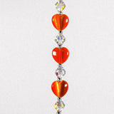 Three orange heart-shaped glass beads with small glass crystal beads in between, strung on stainless steel, hanging vertically against white background.