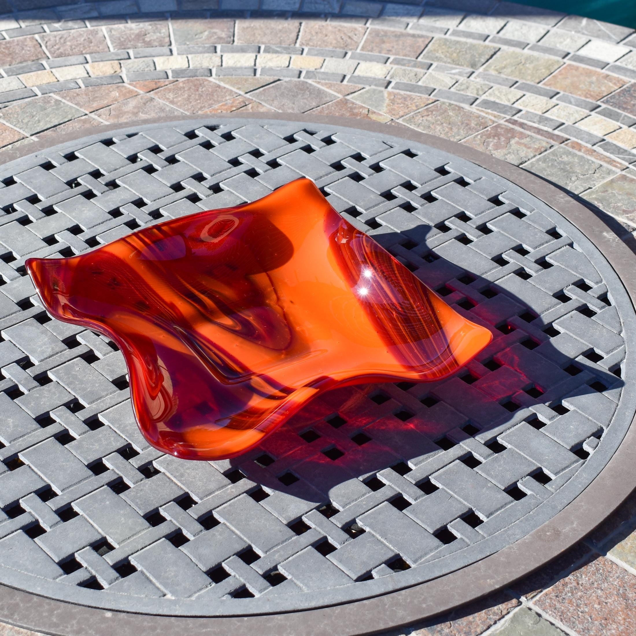 Large square glass bowl with wavy edges and a square center foot, viewed at an angle sitting on a stone table.