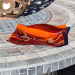 Large square glass bowl with wavy edges and a square center foot, viewed at an angle sitting on a stone table.