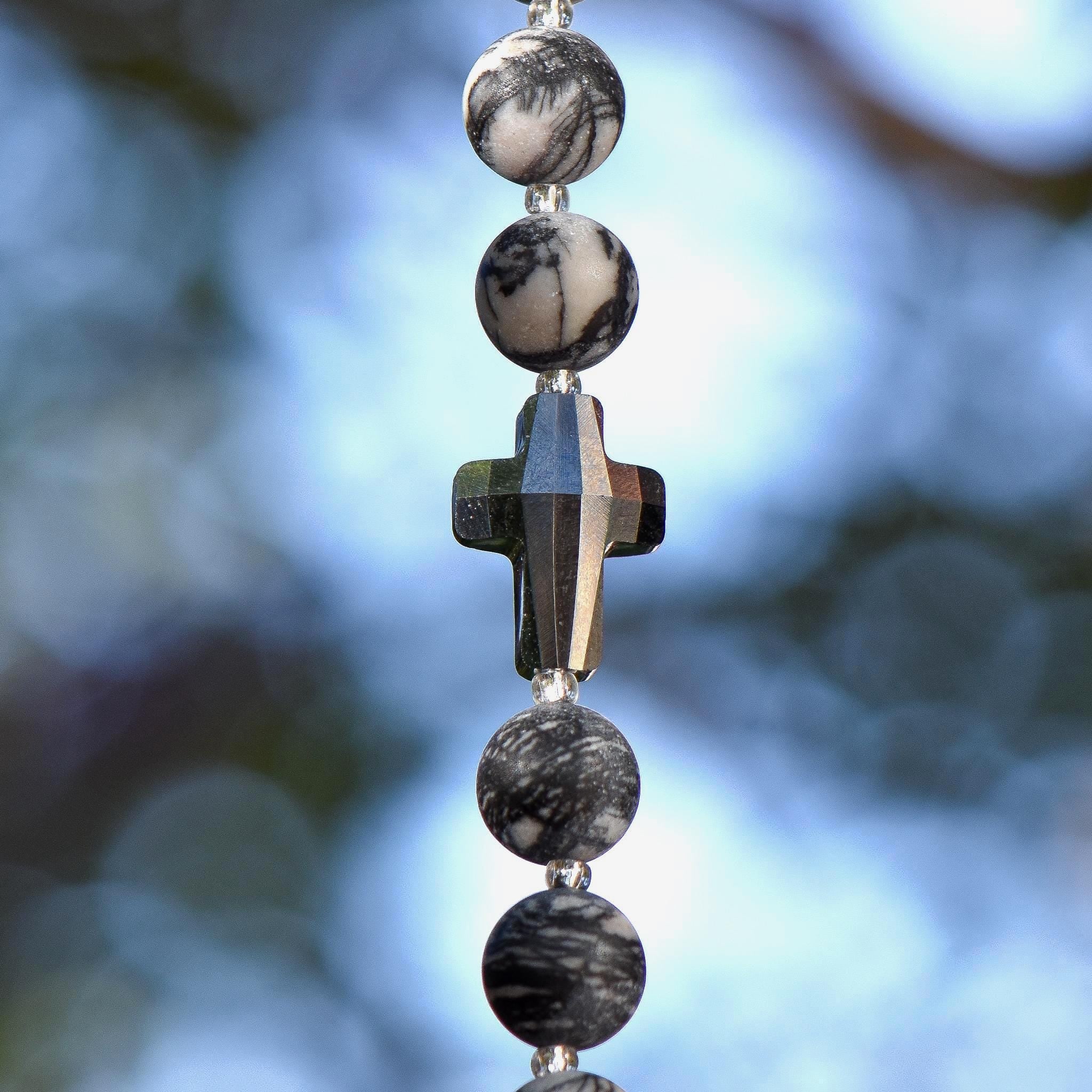 Silvery gray crystal cross bead strung on wire and hanging vertically, flanked by round jasper stone beads.