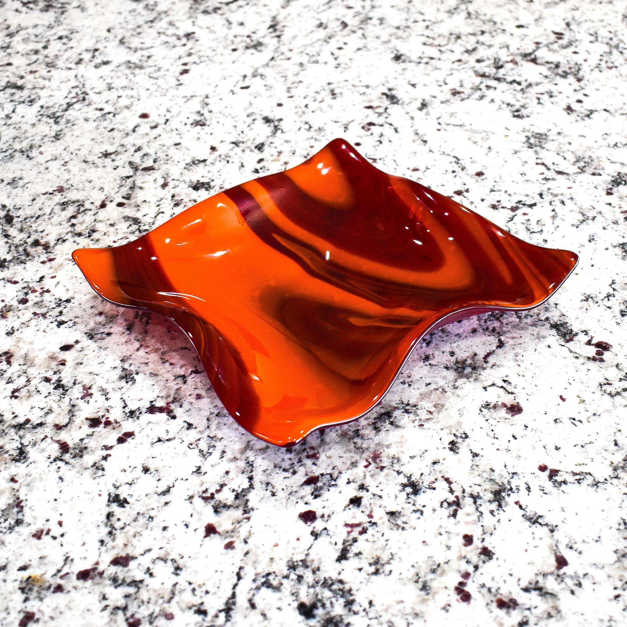 Large square glass bowl with wavy edges and a square center foot, viewed at an angle sitting on gray speckled counter top, inside.