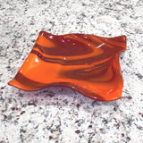 Large square glass bowl with wavy edges and a square center foot, viewed from an angle while sitting on a gray speckled stone countertop, inside.