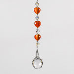 A crystal sun catcher with three orange heart-shaped beads. The suncatcher ends with a clear crystal ball.