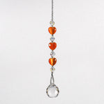A crystal sun catcher with three orange heart-shaped beads. The suncatcher ends with a clear crystal ball.