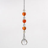 A crystal sun catcher with three orange heart-shaped beads. The suncatcher ends with a clear crystal ball.