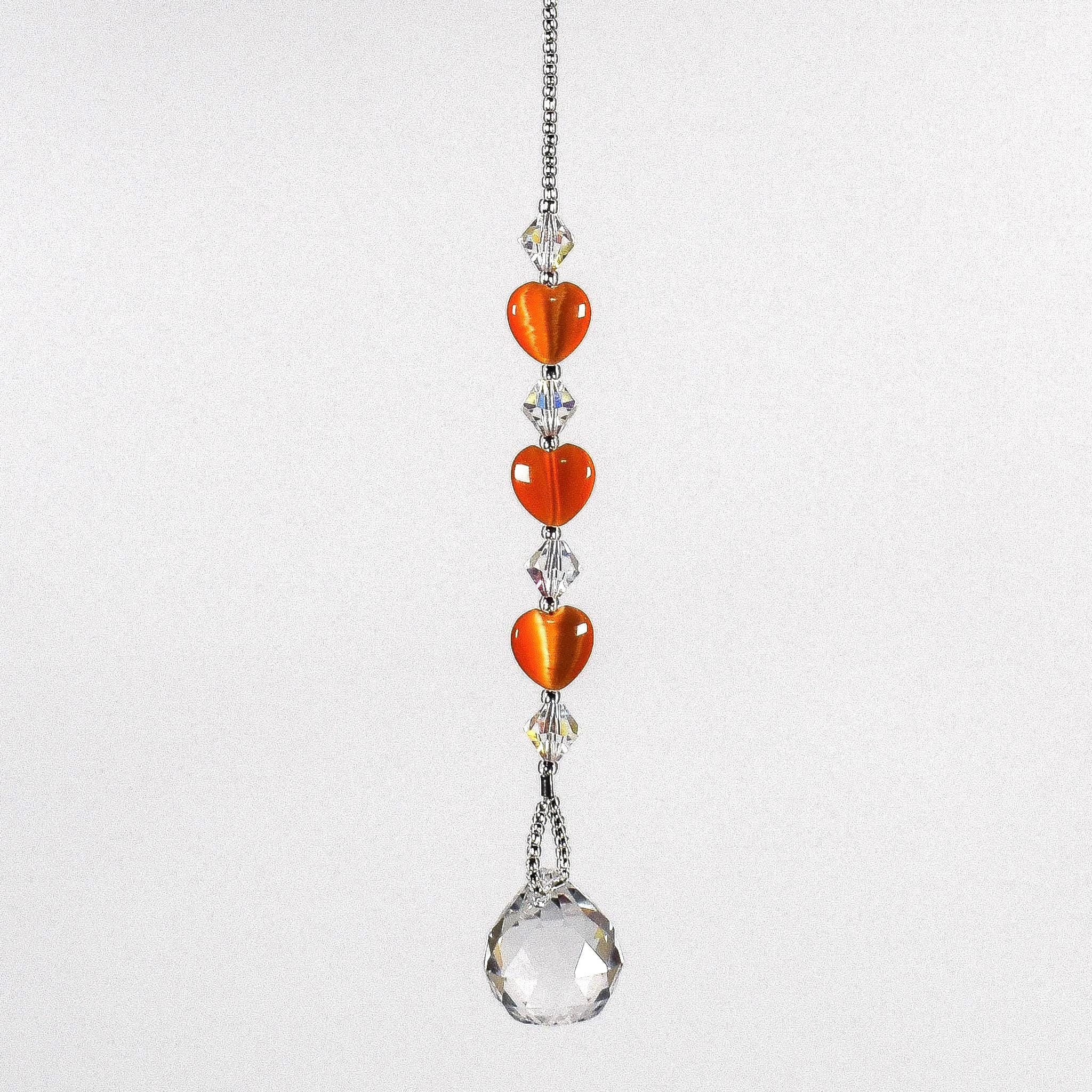 A crystal sun catcher with three orange heart-shaped beads. The suncatcher ends with a clear crystal ball.