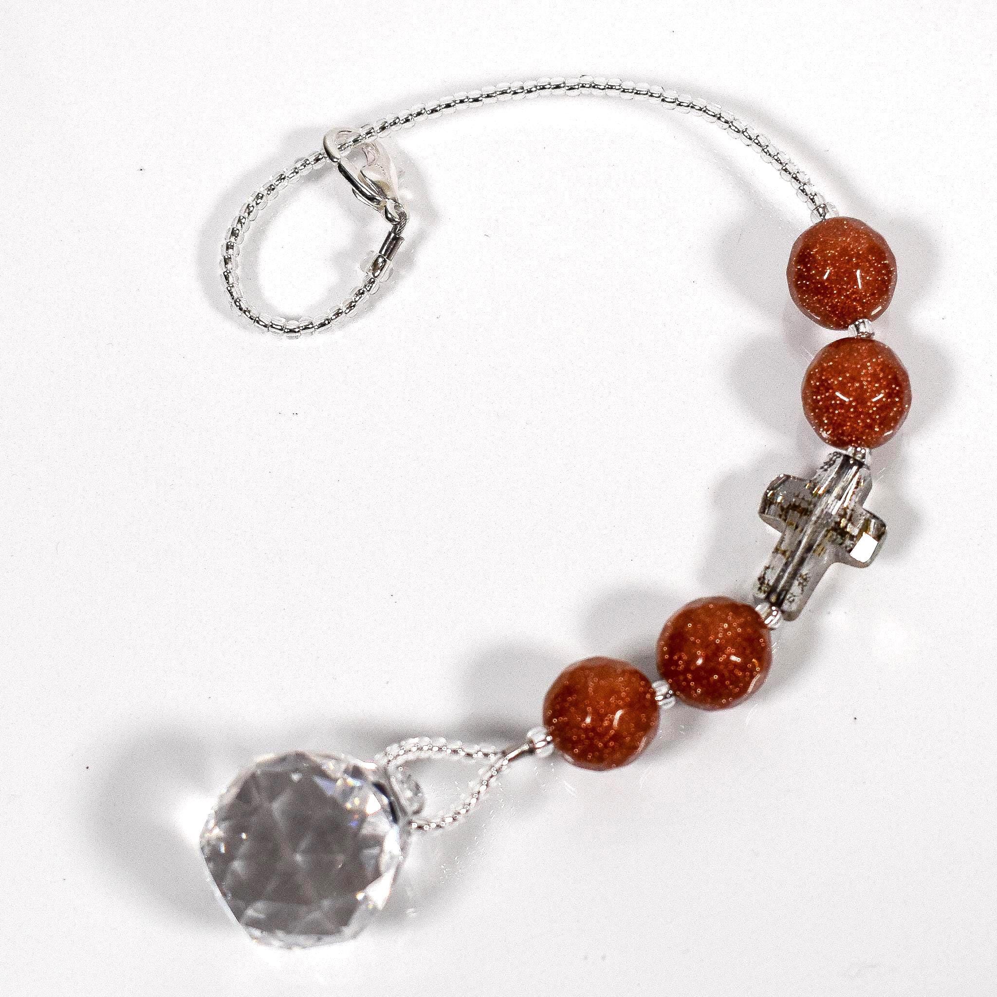 Four round goldstone beads flanking crystal cross bead in gold patina, anchored by small crystal prism, coiled on white surface.