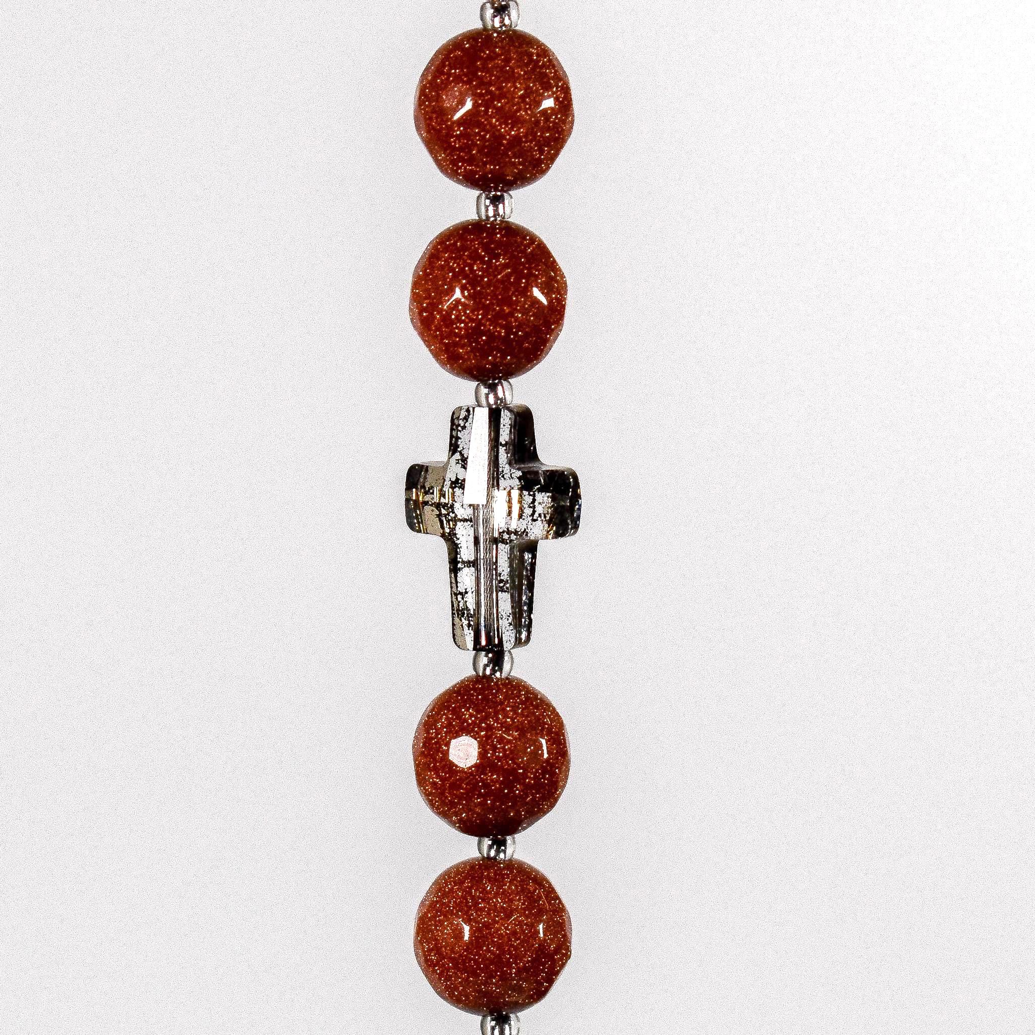 Four round goldstone beads flanking crystal cross bead in gold patina, hanging vertically against white background.