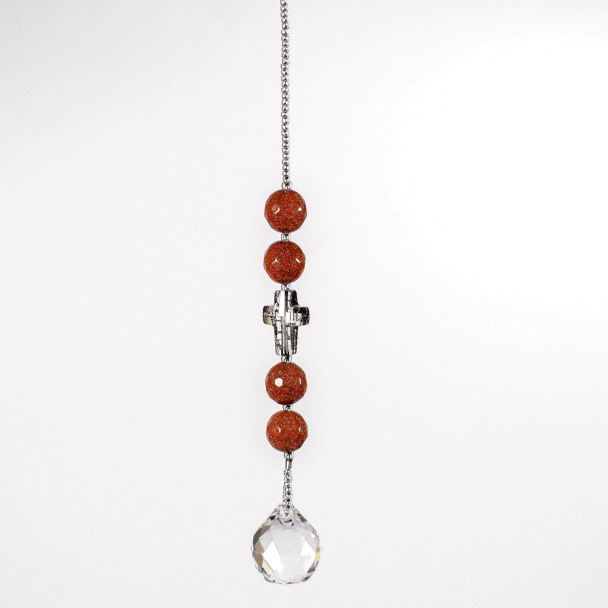 Small sun catcher hanging in front of white background with 4 goldstone beads flanking a golden glass crystal cross. Attached to a round glass crystal prism.
