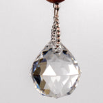 A clear crystal ball hanging from a wire covered in silver-lined seed beads. The crystal ball is faceted and reflects light, creating a rainbow effect.