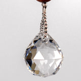A clear crystal ball hanging from a wire covered in silver-lined seed beads. The crystal ball is faceted and reflects light, creating a rainbow effect.