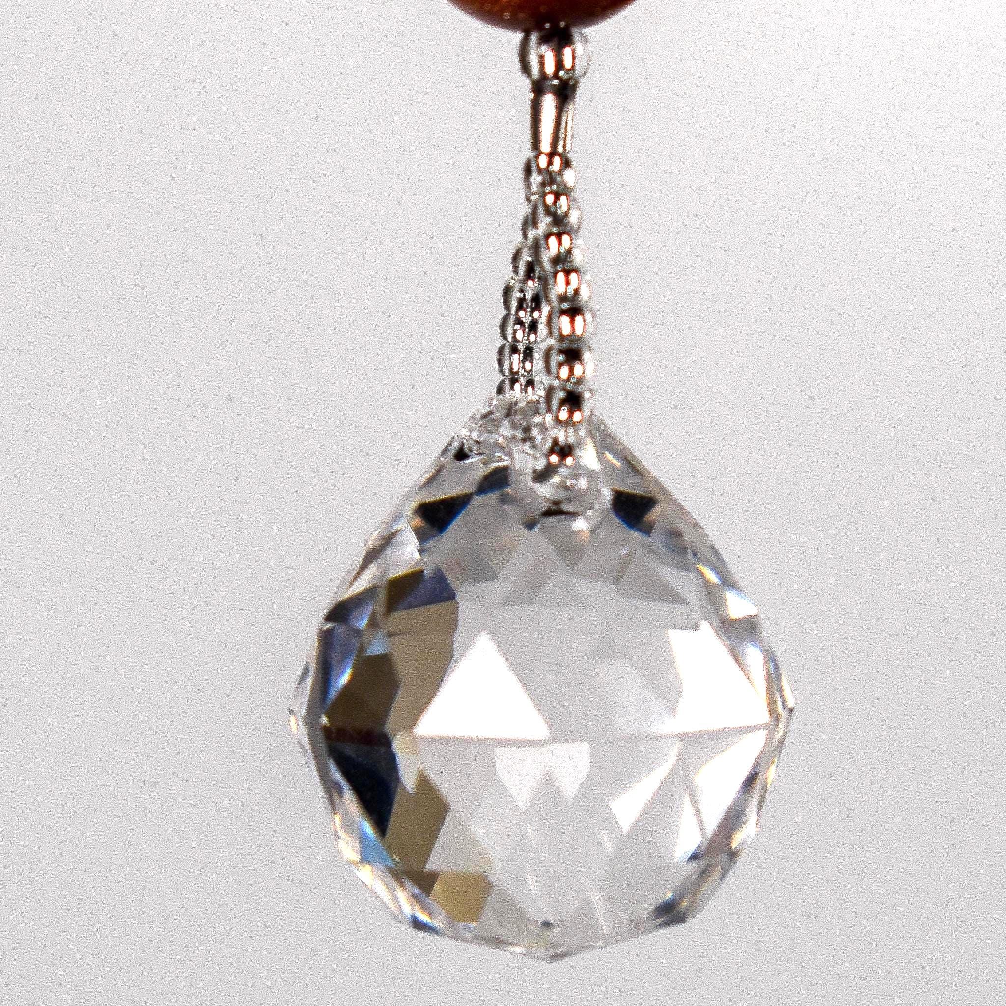 A clear crystal ball hanging from a wire covered in silver-lined seed beads. The crystal ball is faceted and reflects light, creating a rainbow effect.