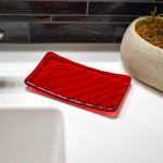 Cherry red glass soap dish with wave texture pattern sitting next to sink in bathroom.