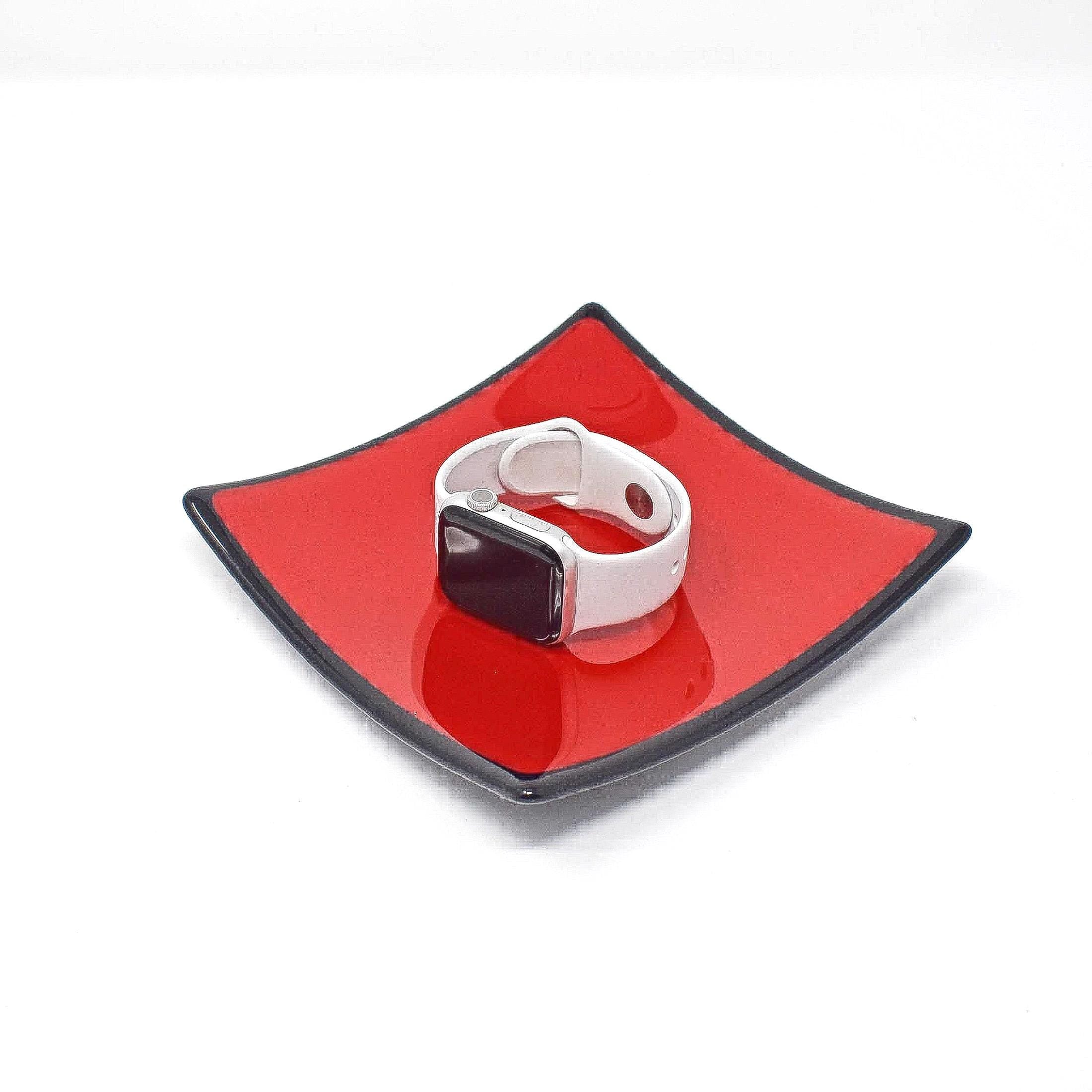 A white Apple Watch with a white band on a red square plate with a black rim.