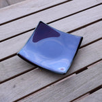 Dusty Violet Purple fused glass tray with black trim sitting on wooden table. Tray is 6" square.