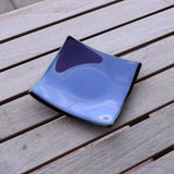 Dusty Violet Purple fused glass tray with black trim sitting on wooden table. Tray is 6" square.