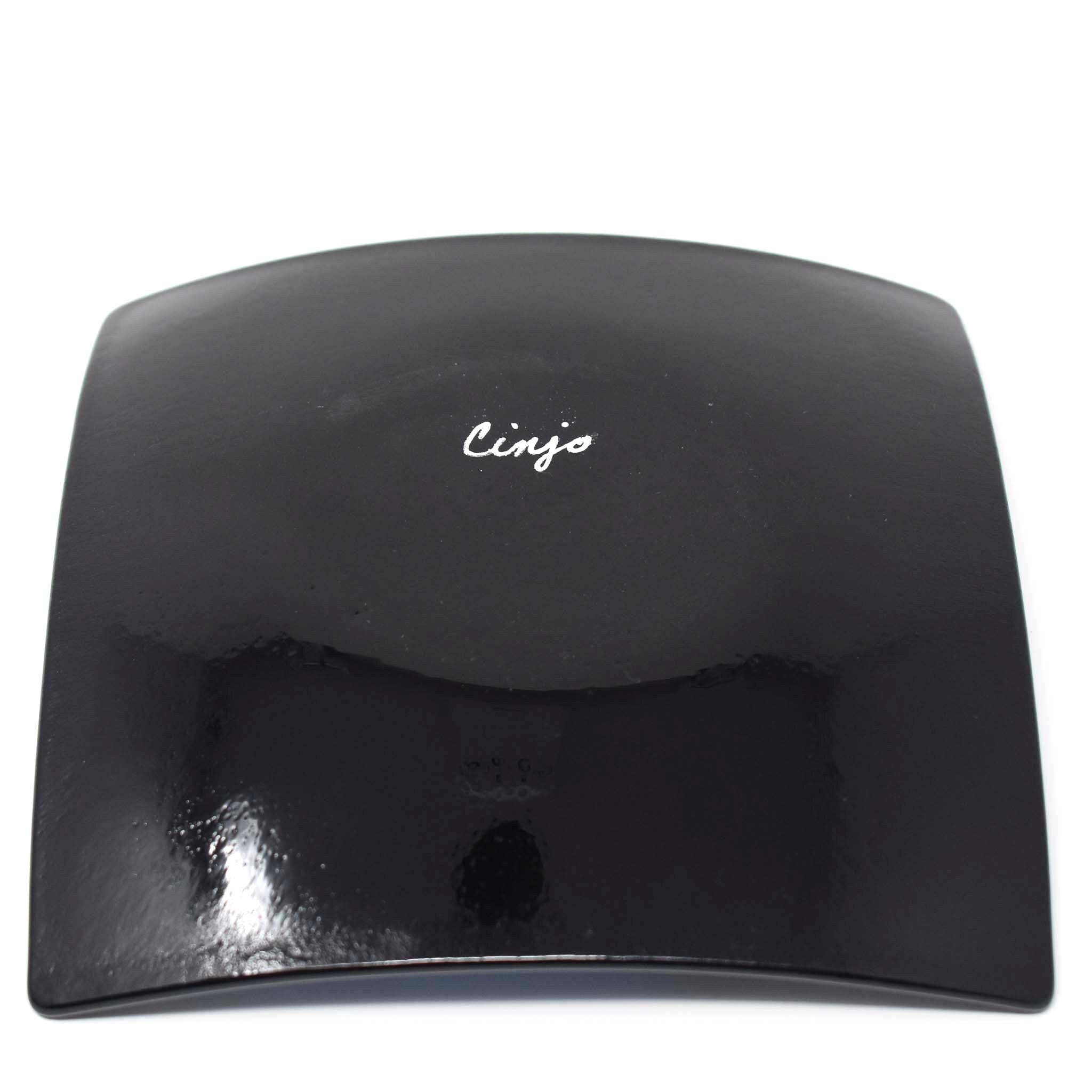 Solid black backside of 6" fused glass tray with signature of "Cinjo". On white background.