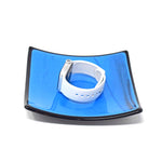 Six inch square glass tray. Center of tray is a medium blue with black streaks. Trim is solid black. White apple watch in center of tray. Tray is on white background.