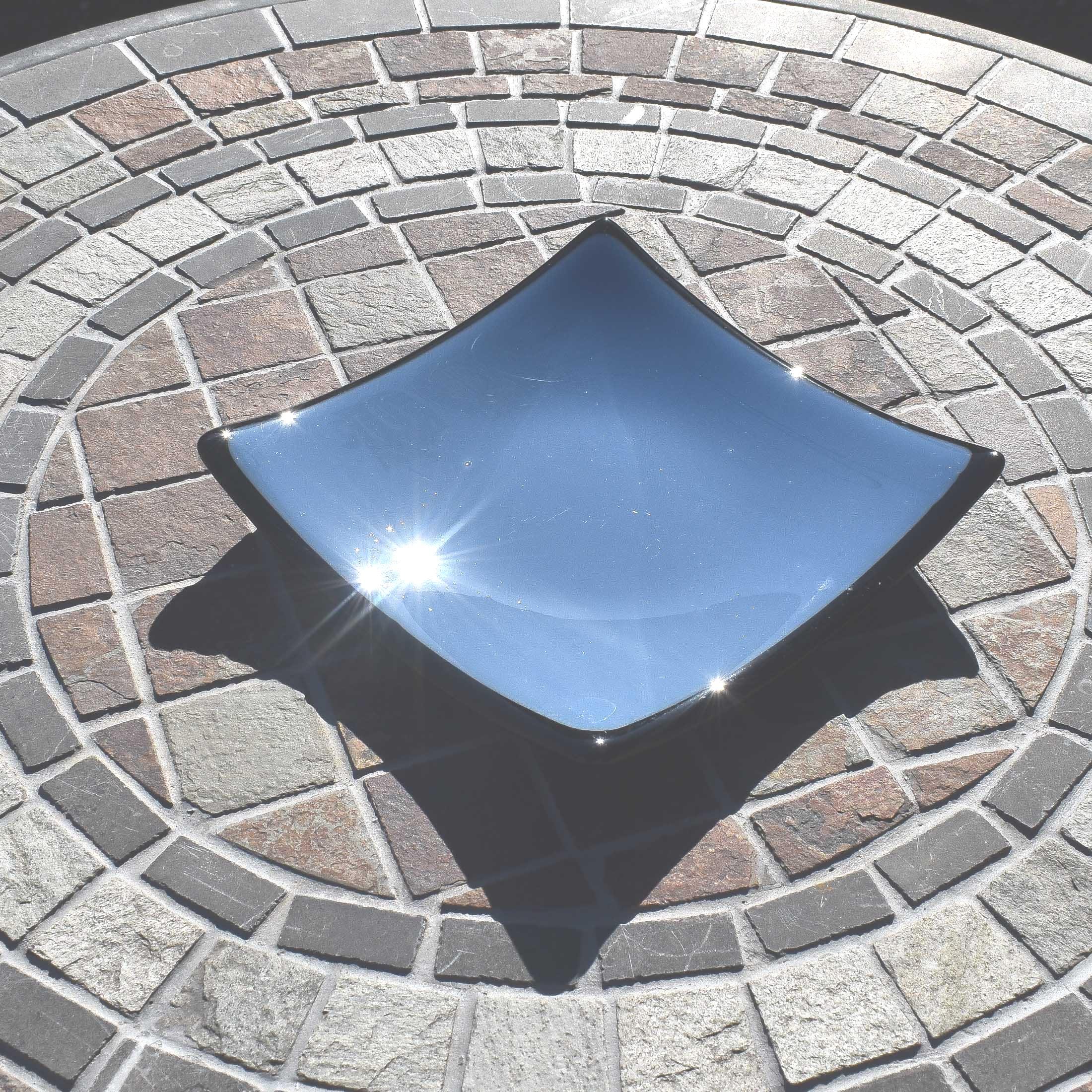 Chambray Blue fused glass dish with black trim and black base. Square with a slight slope at each corner. Sitting on stone table.