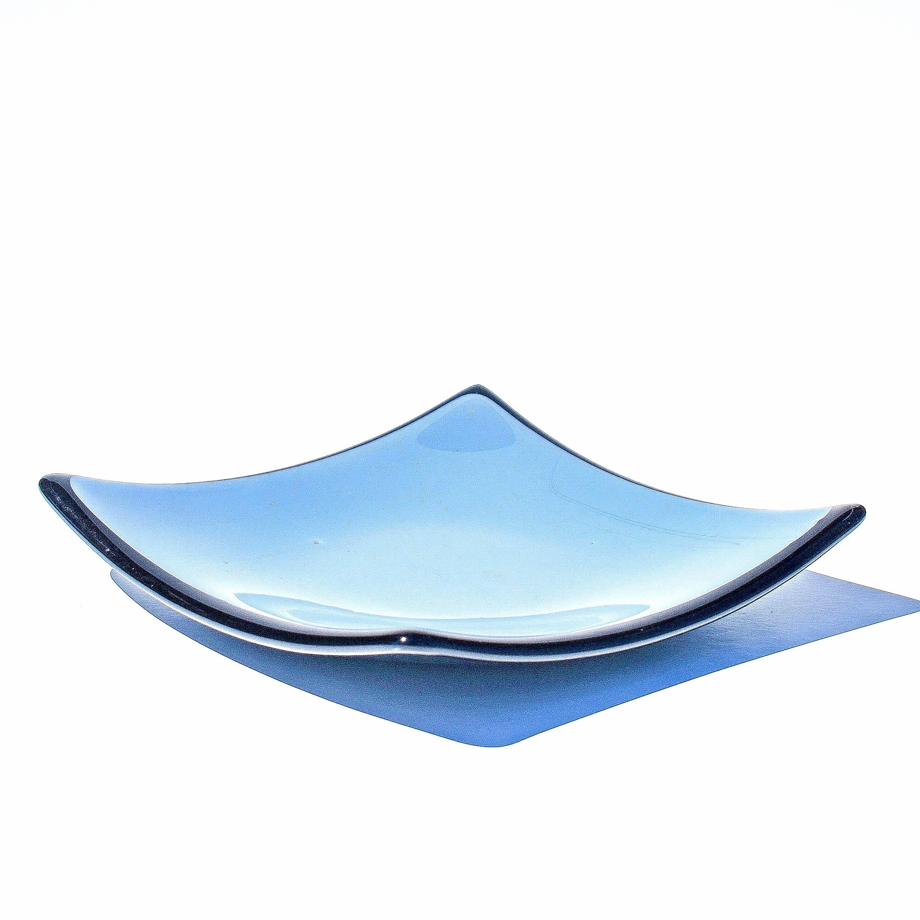 Denim blue square glass dish with black trim and slightly sloped corners, viewed from the side in front of a white background.