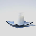 A white frosted glass candle holder with a blue and black wavy glass saucer.