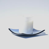 A white frosted glass candle holder with a blue and black wavy glass saucer.