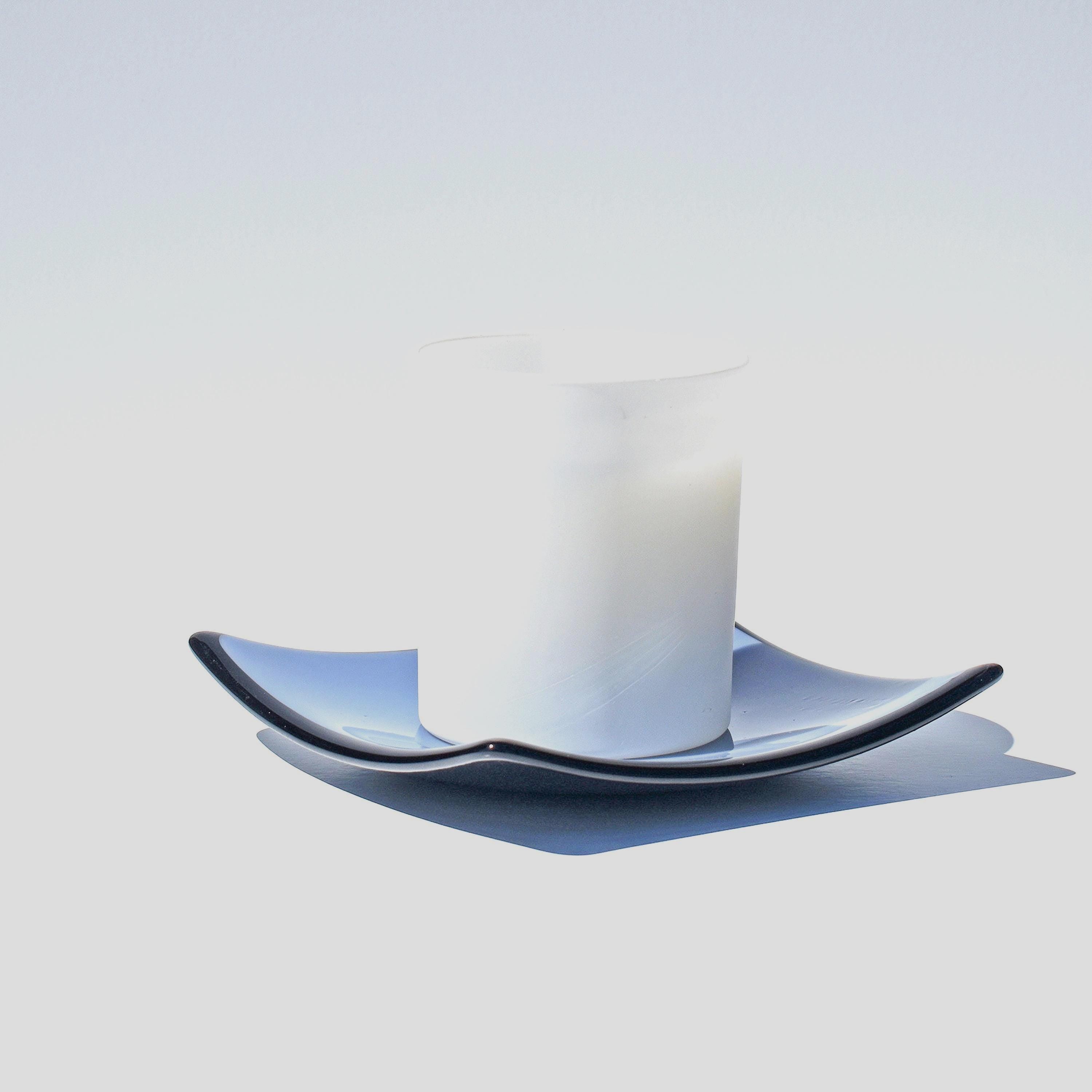 A white frosted glass candle holder with a blue and black wavy glass saucer.