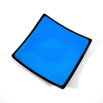 Square fused glass dish with solid blue center, black trim and black base, sitting white surface.