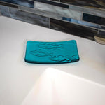 Glass soap dish in "Caribbean Blue" glass with swimming fish design sitting near a bathroom sink.