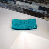 Glass soap dish in "Caribbean Blue" glass with swimming fish design sitting near a bathroom sink.