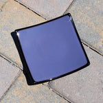 Dusty Violet Purple fused glass tray with black trim sitting on pavers in sunlight. Tray is 6" square.
