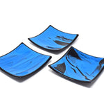 Three different six inch square glass trays. Center of each tray is a medium blue with black streaks. Trim is solid black. On white background.