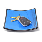Set of keys on six inch square glass tray. Center of tray is a medium blue with black streaks. Trim is solid black.