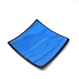 Six inch fused glass square tray with blue and black center, trimmed with black and with a black base, white background.