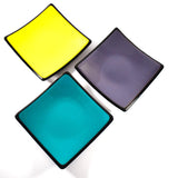 Top view of 3 different colored 6" fused glass square trays: Yellow, Purple and Teal Green.