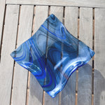 Blue fused glass wave bowl with flowing lines in transparent blue fused glass, shown empty on a slatted wooden table.