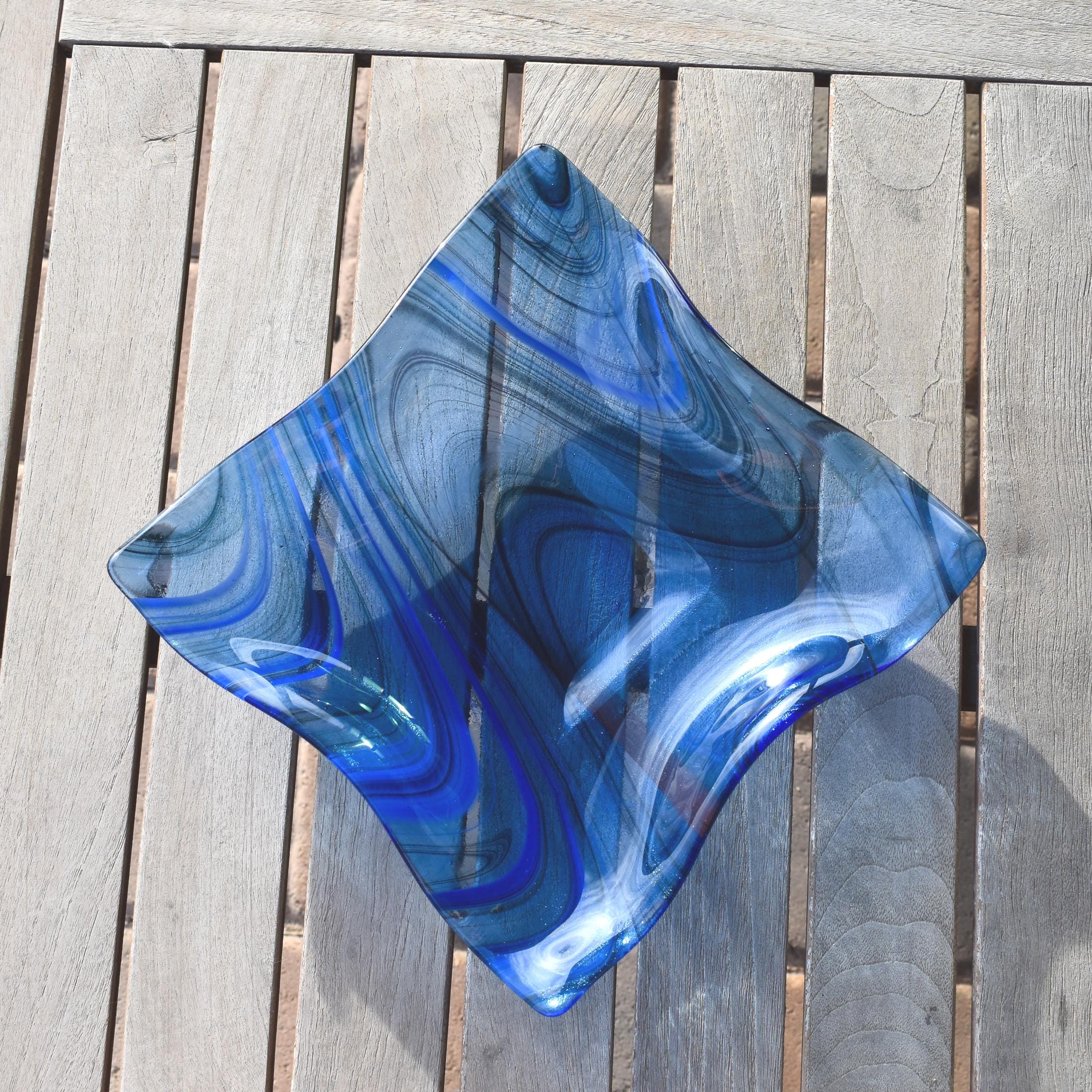 Blue fused glass wave bowl with flowing lines in transparent blue fused glass, shown empty on a slatted wooden table.