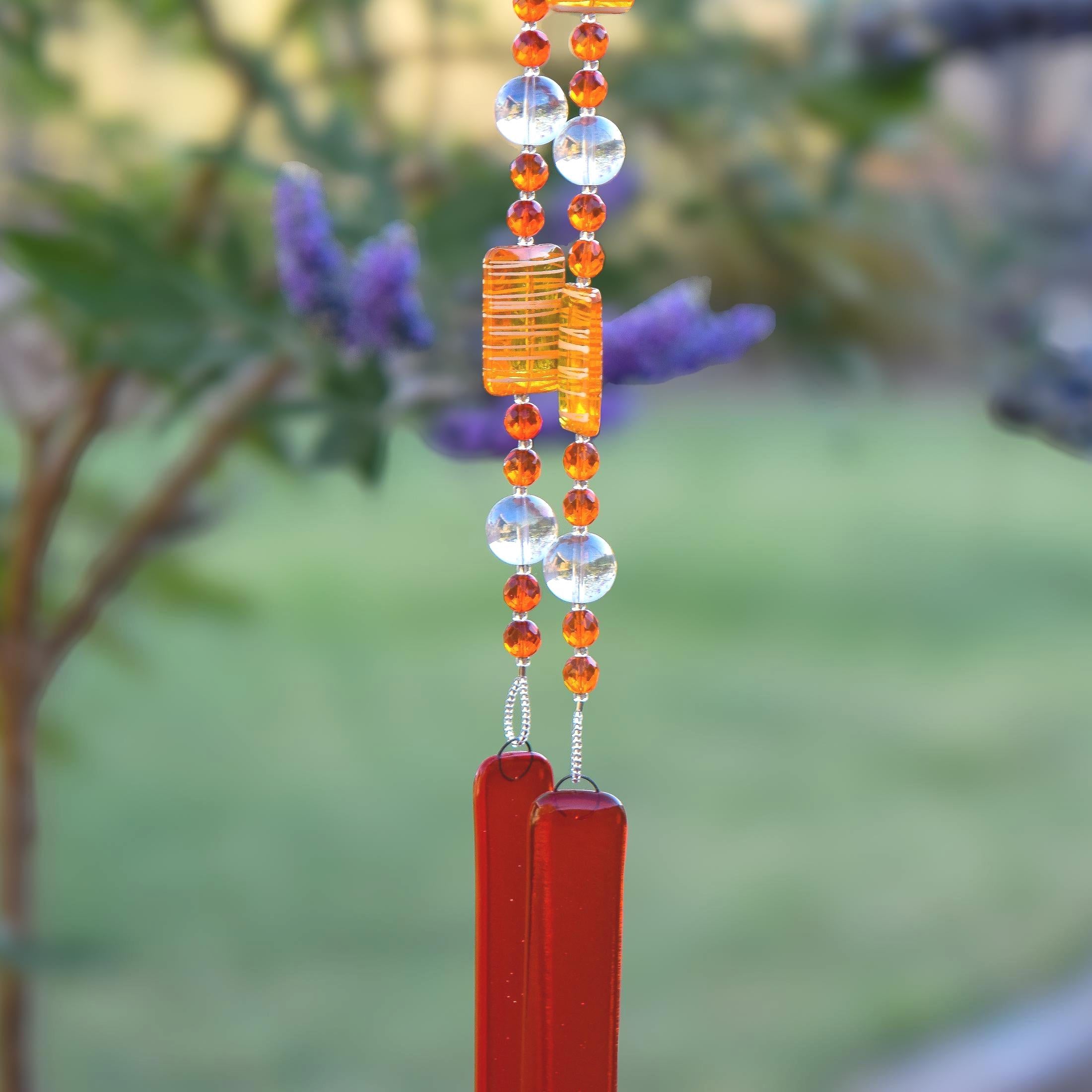 Orange wind chime hanging from tree. Chime is made of fused glass, glass beads, stainless steel wire and acrylic rectangular beads.