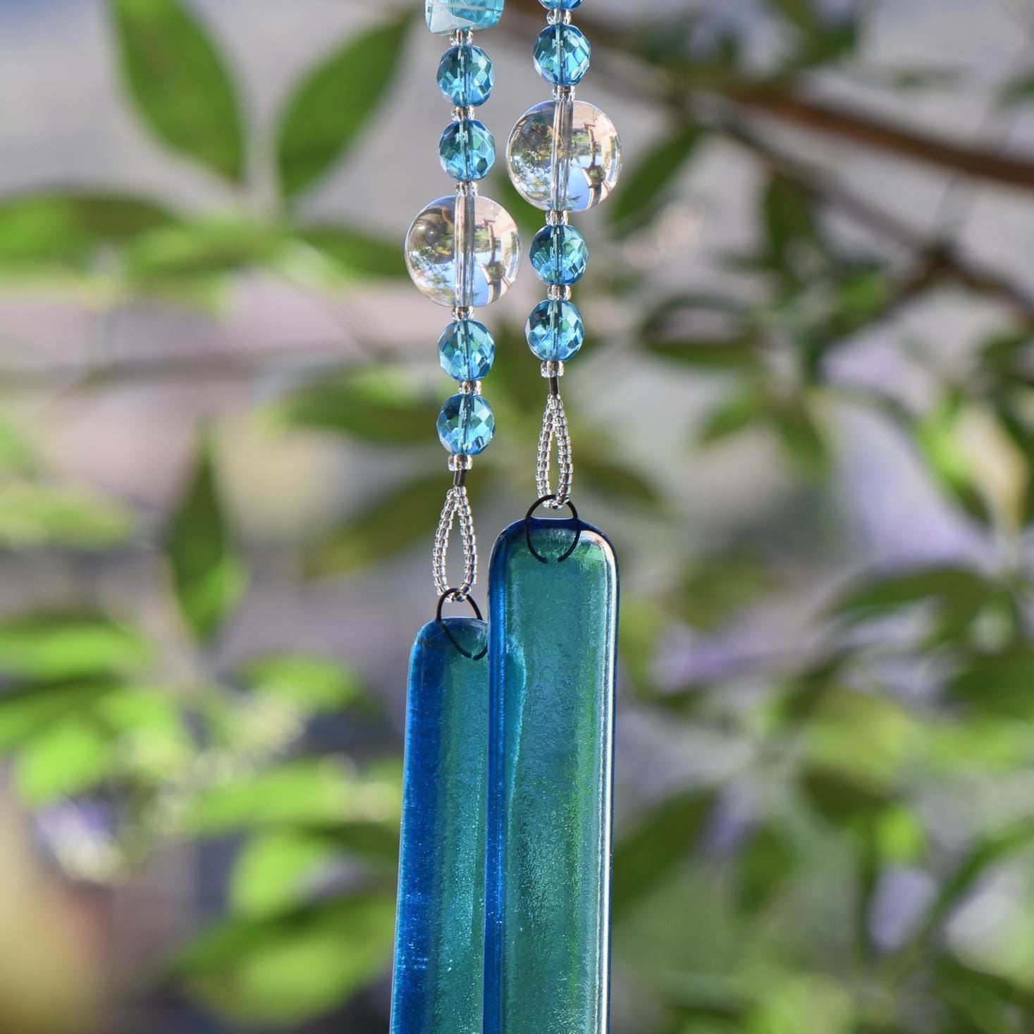 Blue wind chime hanging from tree. Chime is made of fused glass, glass beads, stainless steel wire and acrylic rectangular beads.