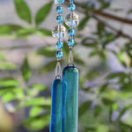 Blue wind chime hanging from tree. Chime is made of fused glass, glass beads, stainless steel wire and acrylic rectangular beads.